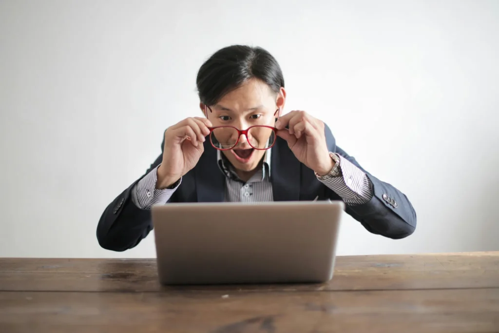 Homme à lunette en chemise regardant son ordinateur de façon stupéfaite.