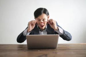 Homme à lunette en chemise regardant son ordinateur de façon stupéfaite.