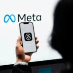Personne tenant un téléphone avec l’application Threads ouverte, devant le logo Meta, illustrant la communication numérique.