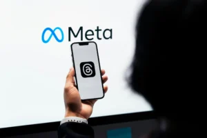 Personne tenant un téléphone avec l’application Threads ouverte, devant le logo Meta, illustrant la communication numérique.