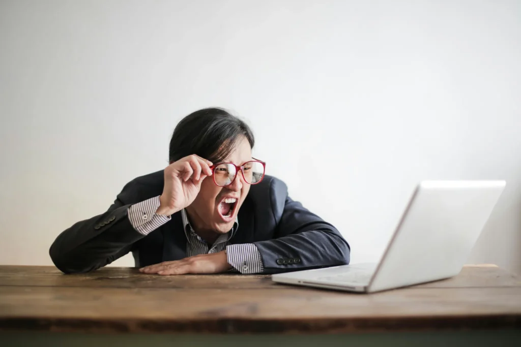 Homme à lunettes criant devant son ordinateur, illustrant la frustration et les défis en communication digitale.