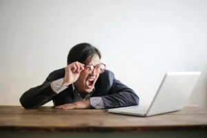 Homme à lunettes criant devant son ordinateur, illustrant la frustration et les défis en communication digitale.