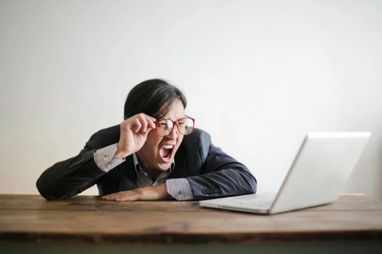 Homme à lunettes criant devant son ordinateur, illustrant la frustration et les défis en communication digitale.