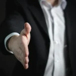 Homme en costume tendant la main, symbole d’accord, de partenariat ou d’accueil professionnel.
