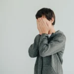 Jeune garçon stressé se cachant le visage, illustrant les blocages en communication ou le manque de confiance