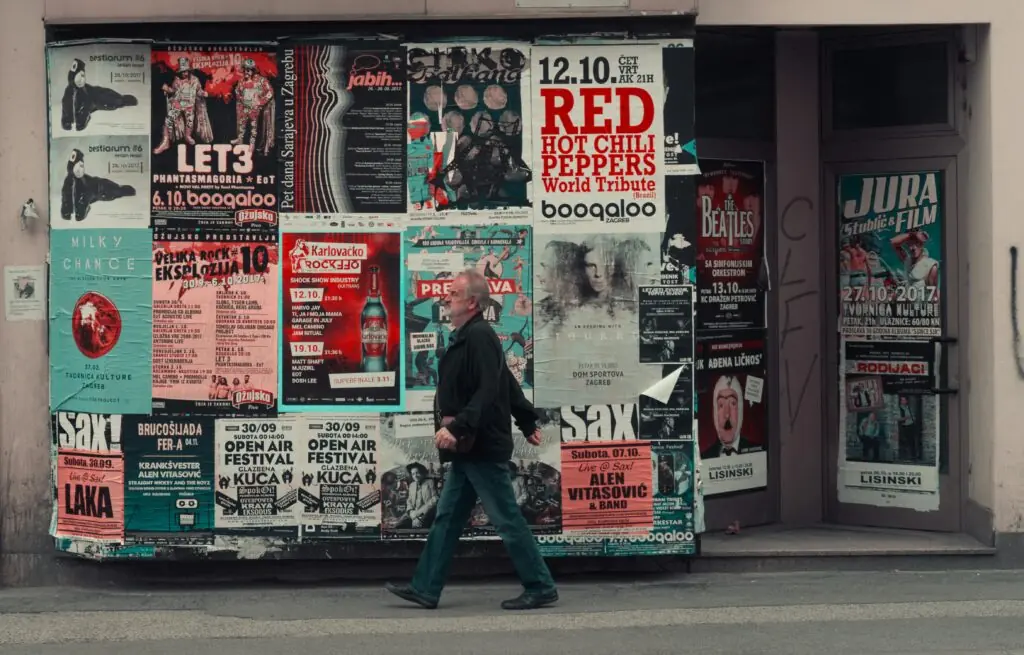 Homme marchant dans la rue devant des affiches de communication papier.