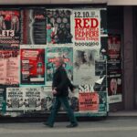 Homme marchant dans la rue devant des affiches de communication papier.