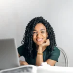 Femme souriante derrière son ordinateur pour représenter une communication digitale fluide et efficace.
